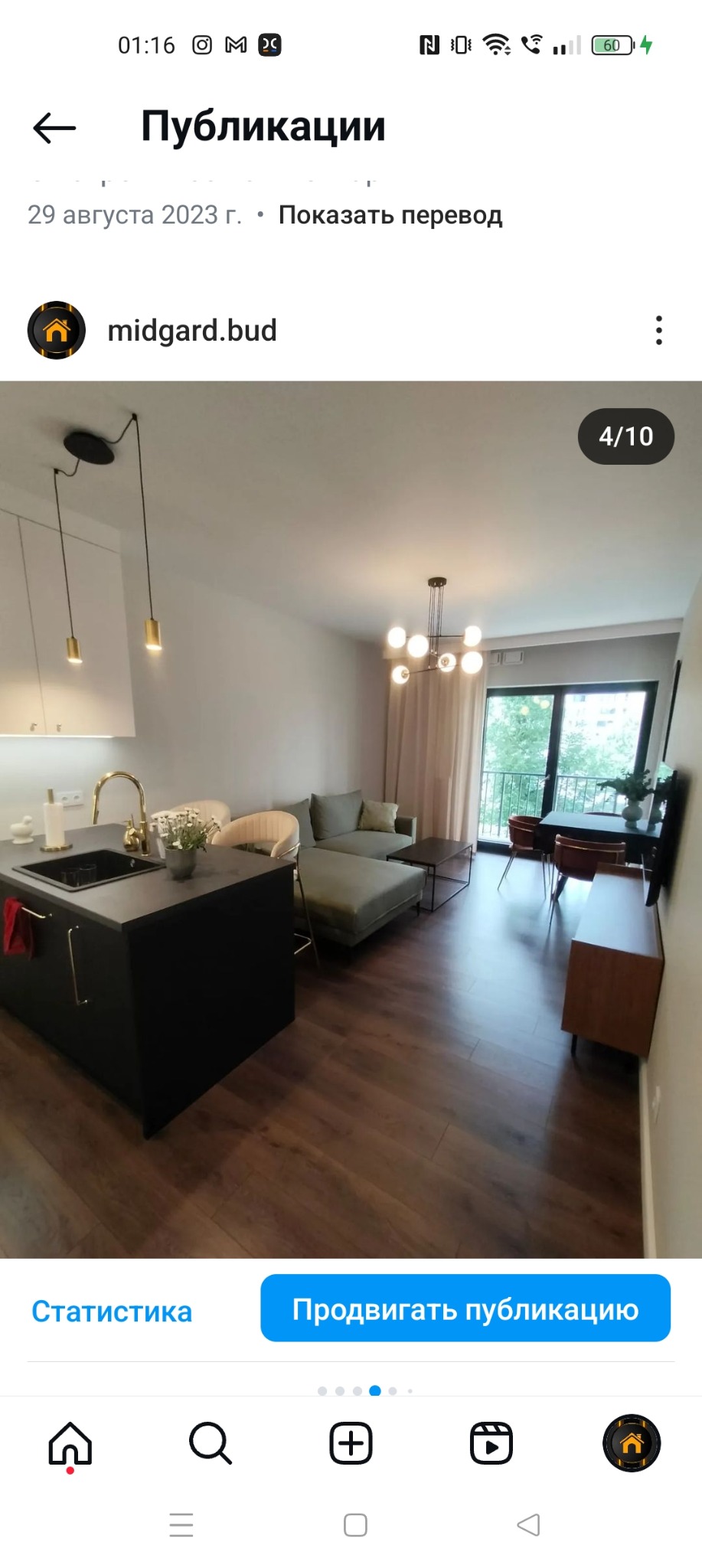 Nowoczesne wnętrze mieszkania z otwartą kuchnią, wyspą kuchenną z czarnym blatem i złotą armaturą, drewnianą podłogą, szarą sofą i balkonem z widokiem na zieleń.