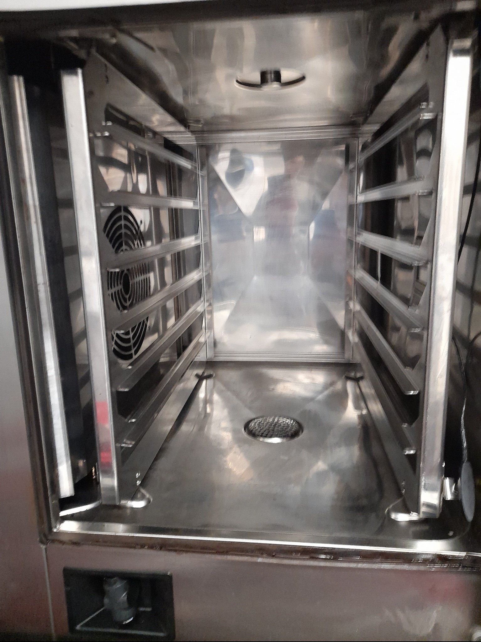 Wnętrze czystego, nierdzewnego pieca konwekcyjnego z wentylatorem i prowadnicami na blachy, gotowe do użytku.