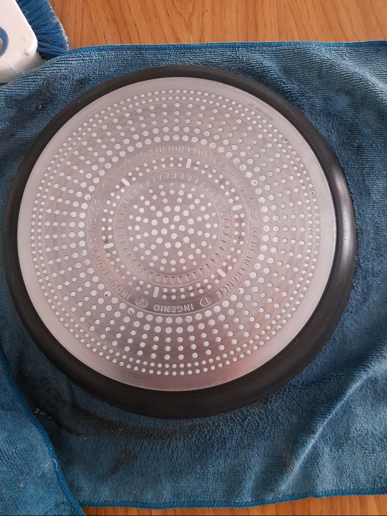 Spód patelni marki Ingenio, po umyciu, leży na niebieskiej ściereczce z mikrofibry. Widoczne napisy: Thermo-Fusion Plus, Made in France, Induction Technology.