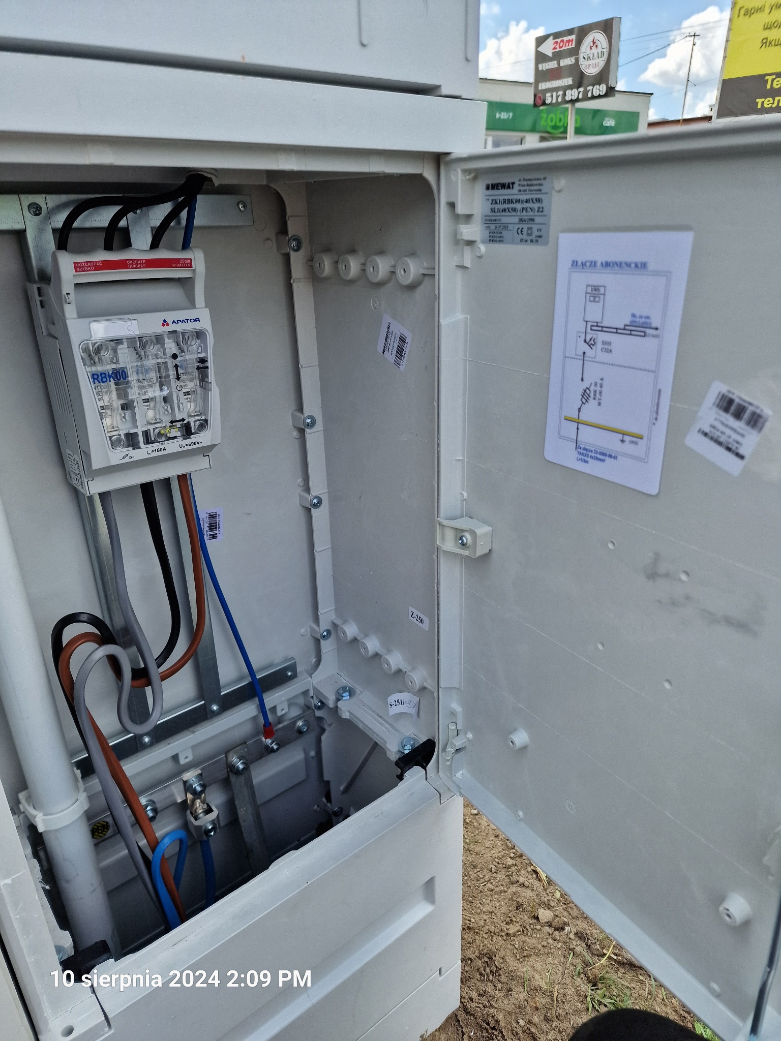 Otwarta skrzynka elektryczna z zamontowanym bezpiecznikiem RBK00 i okablowaniem w Mszczonowie, widoczne schematy i oznaczenia na wewnętrznej stronie drzwiczek.