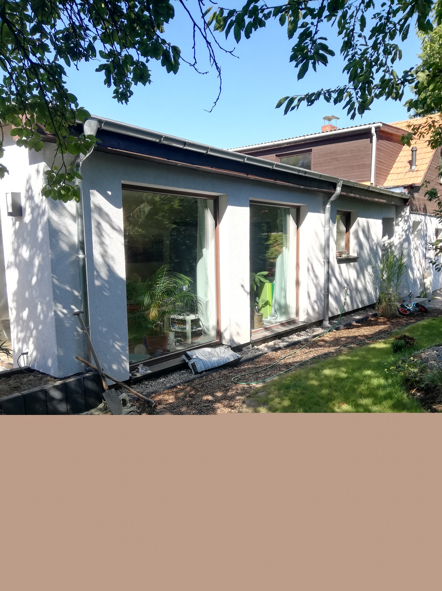 Biały, parterowy budynek z dużymi oknami, widok z zewnątrz, teren wokół w trakcie prac wykończeniowych, widoczne narzędzia i materiały budowlane.