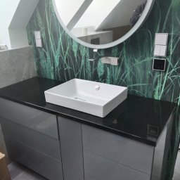 GraniMar - Łazienka z czarnym blatem, białą, kwadratową umywalką, szarą szafką pod umywalką i okrągłym lustrem z podświetleniem LED na ścianie z motywem trawy.