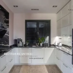 Kuchnia z białymi szafkami i blatem z czarnego kamienia Belvedere Antico o wyraźnym, złotym użyleniu, ekspres do kawy i blender na blacie.