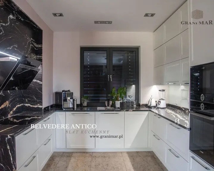 Kuchnia z białymi szafkami i blatem z czarnego kamienia Belvedere Antico o wyraźnym, złotym użyleniu, ekspres do kawy i blender na blacie.