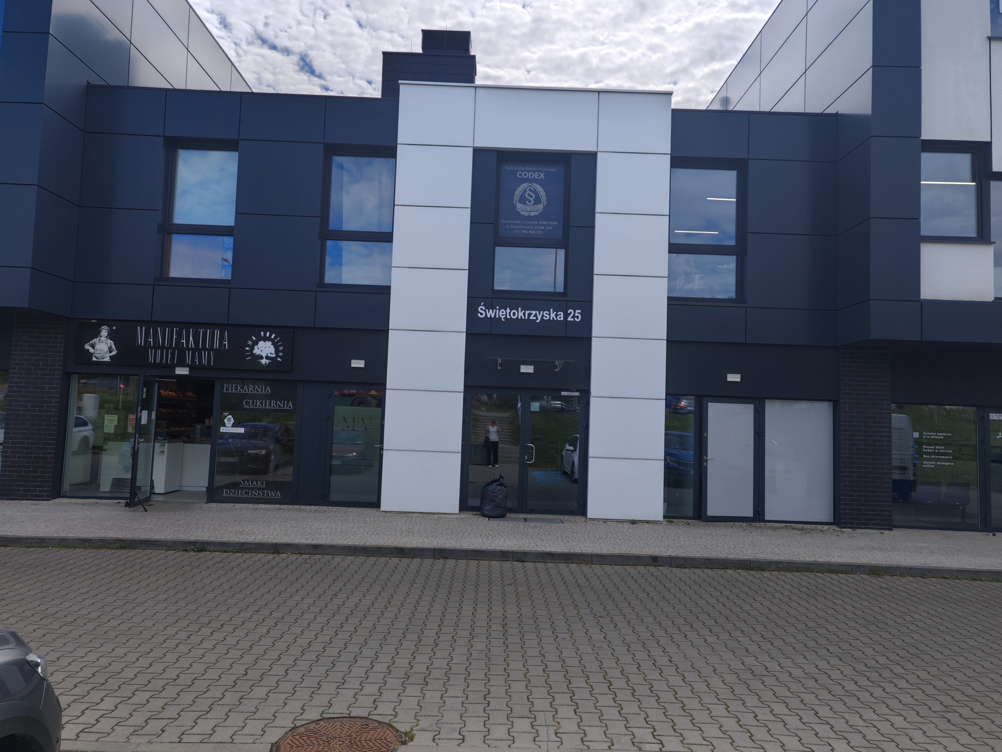 Budynek biurowy z szyldem 'Kancelaria Radcy Prawnego CODEX' i adresem Świętokrzyska 25. Widoczne okna i drzwi wejściowe. Obok piekarnia i cukiernia.