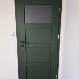 PUERTA DRZWI - Zielone drzwi wewnętrzne z szybą w górnej części, zamontowane w nowym budynku z widocznym gniazdkiem elektrycznym bez obudowy i surową podłogą.