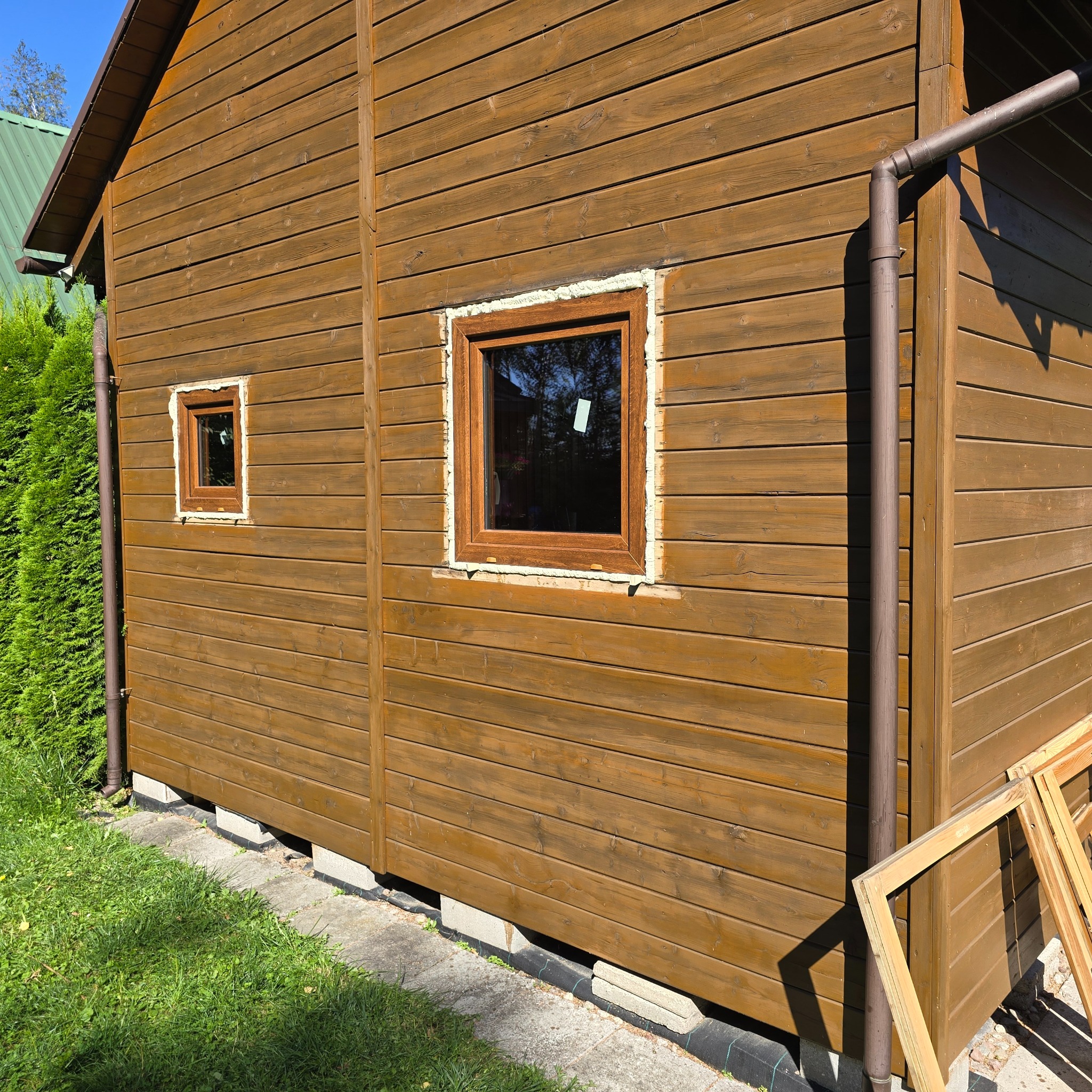 Montaż okna w drewnianym domu, widoczne pianowanie wokół ramy, obok leżą stare ramy okienne.