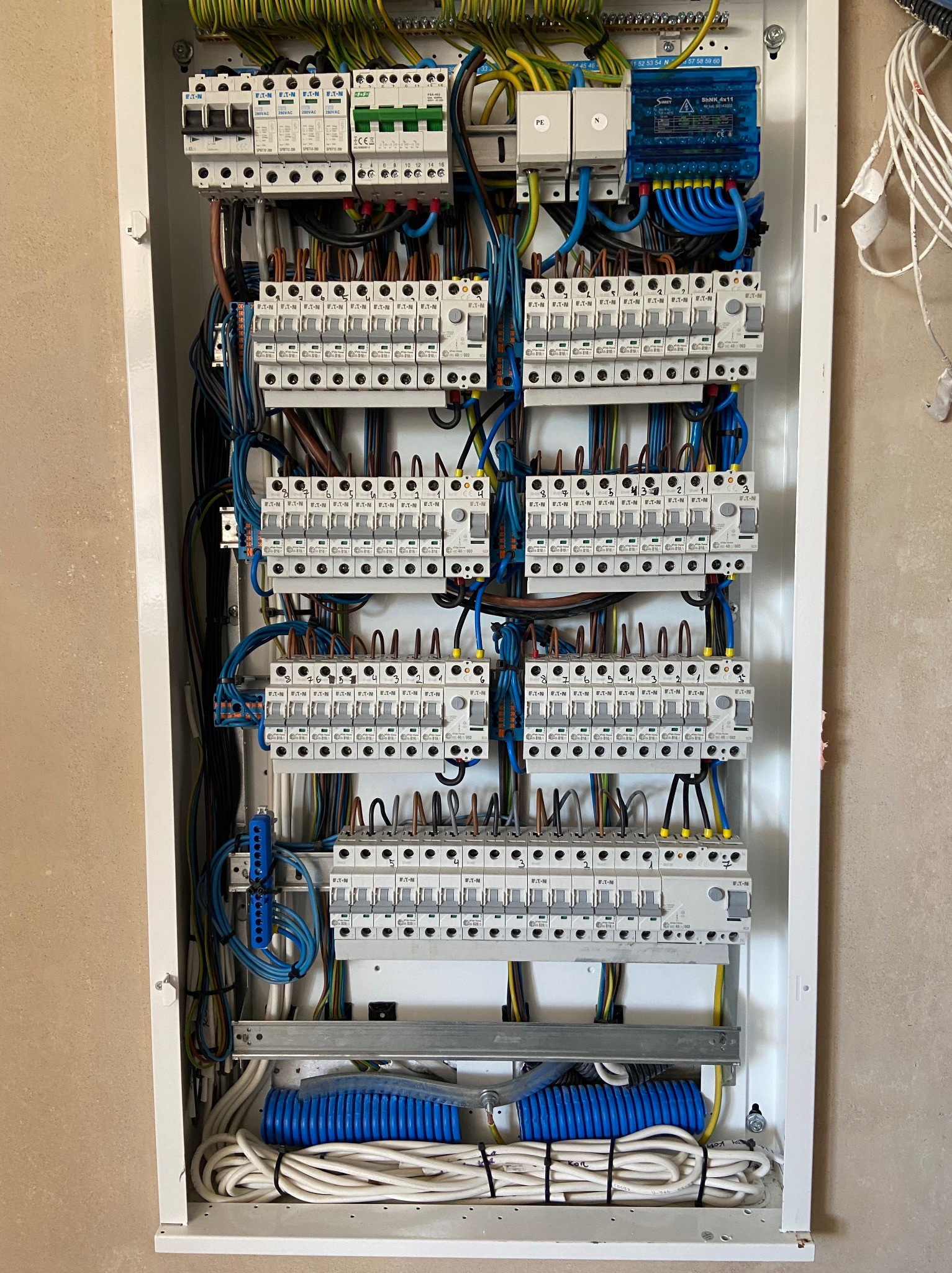 Rozdzielnica elektryczna z zamontowanymi bezpiecznikami i przewodami, widok z bliska na kompletną instalację w białej obudowie.