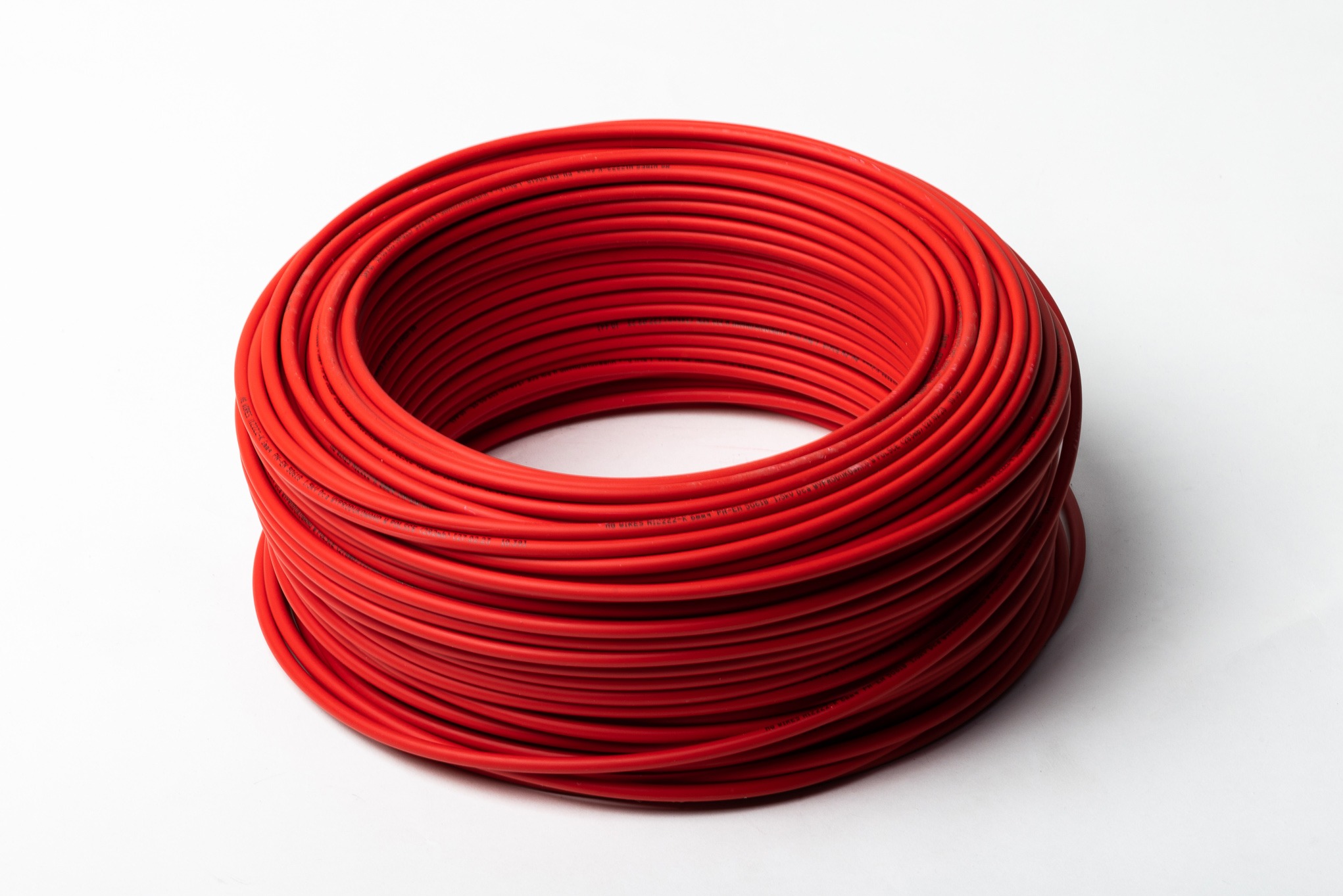 Zwój czerwonego kabla elektrycznego na białym tle, widoczne napisy na izolacji.