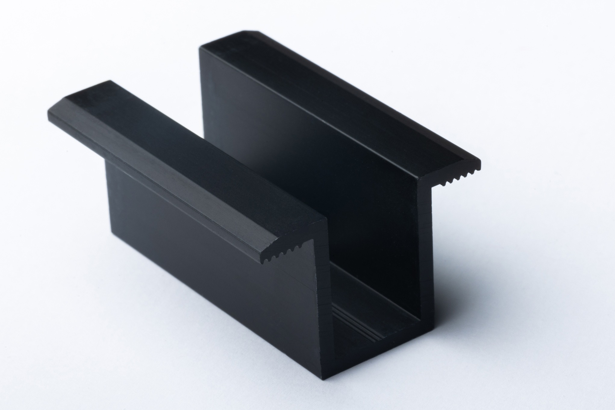 Czarny, aluminiowy profil montażowy z ząbkowaną krawędzią, prawdopodobnie do paneli słonecznych, na białym tle.