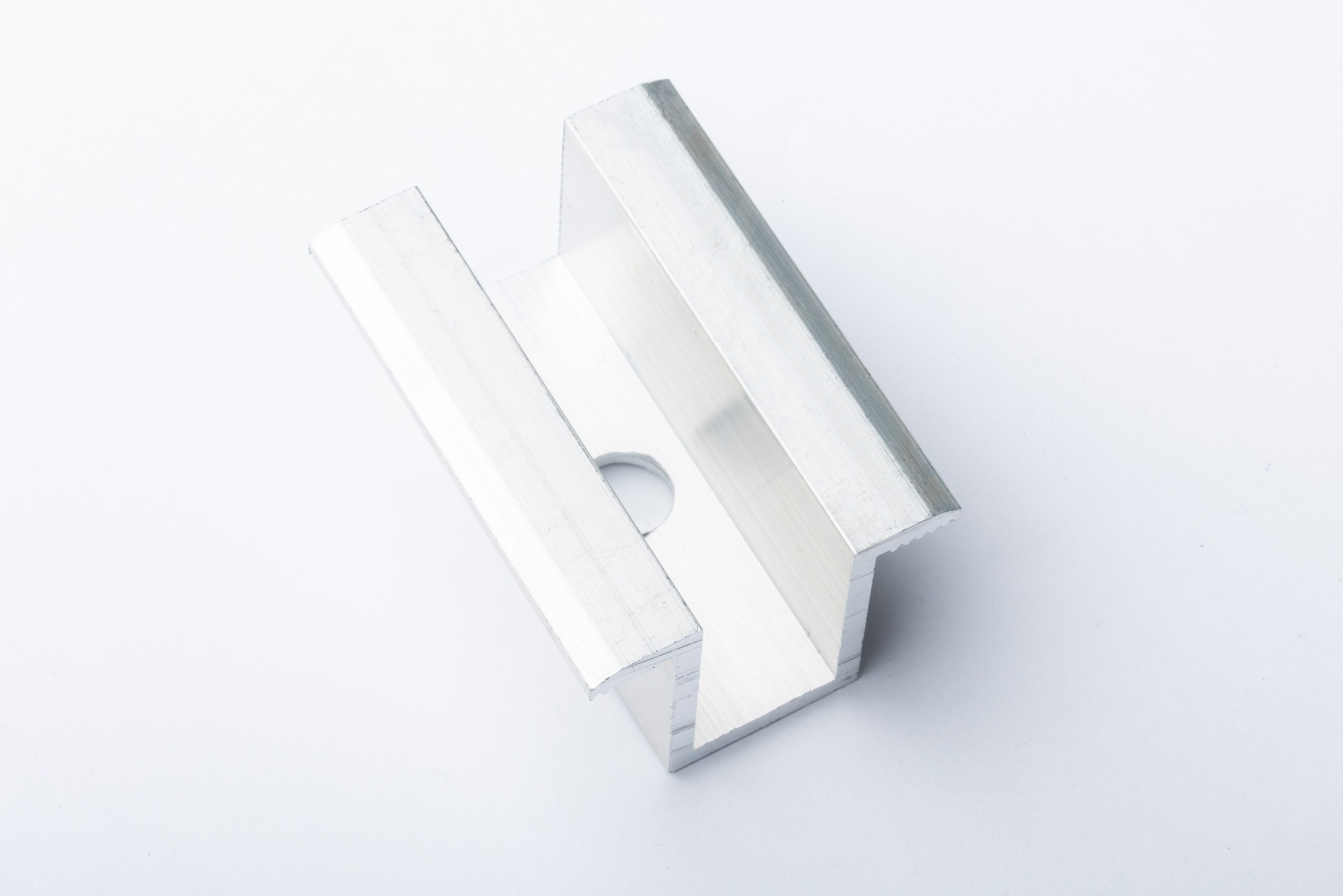 Aluminiowy profil montażowy, prawdopodobnie do paneli słonecznych, z otworem na śrubę, sfotografowany na białym tle.