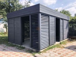 Nowoczesna, grafitowa konstrukcja z poziomych desek, przypominająca altanę lub pawilon ogrodowy, z częściowo otwartymi ścianami z żaluzji, na tle zieleni.