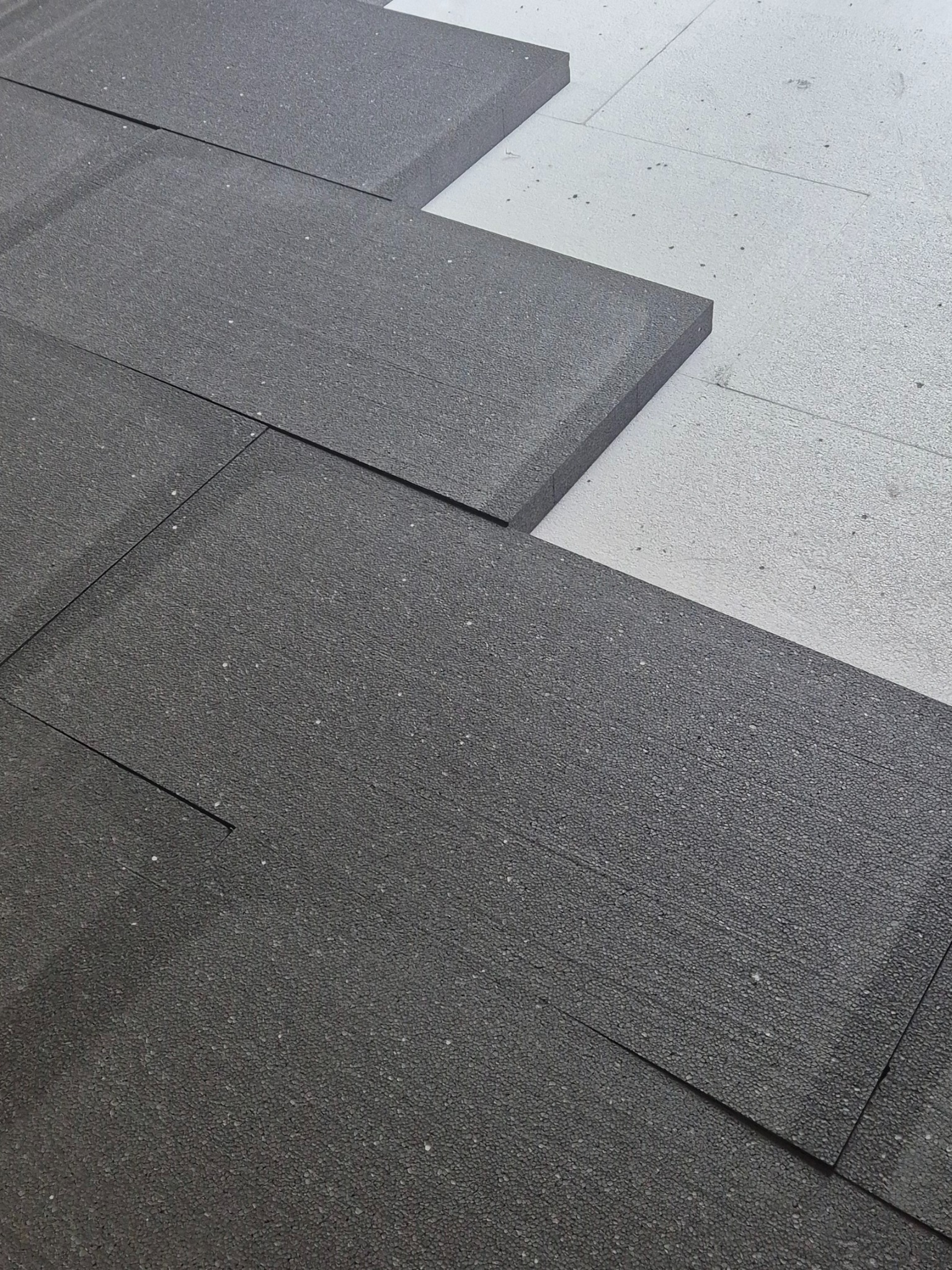 Szare płyty izolacyjne ułożone na białej powierzchni, prawdopodobnie podczas montażu ogrzewania podłogowego. Widok z góry, bliski kadr.