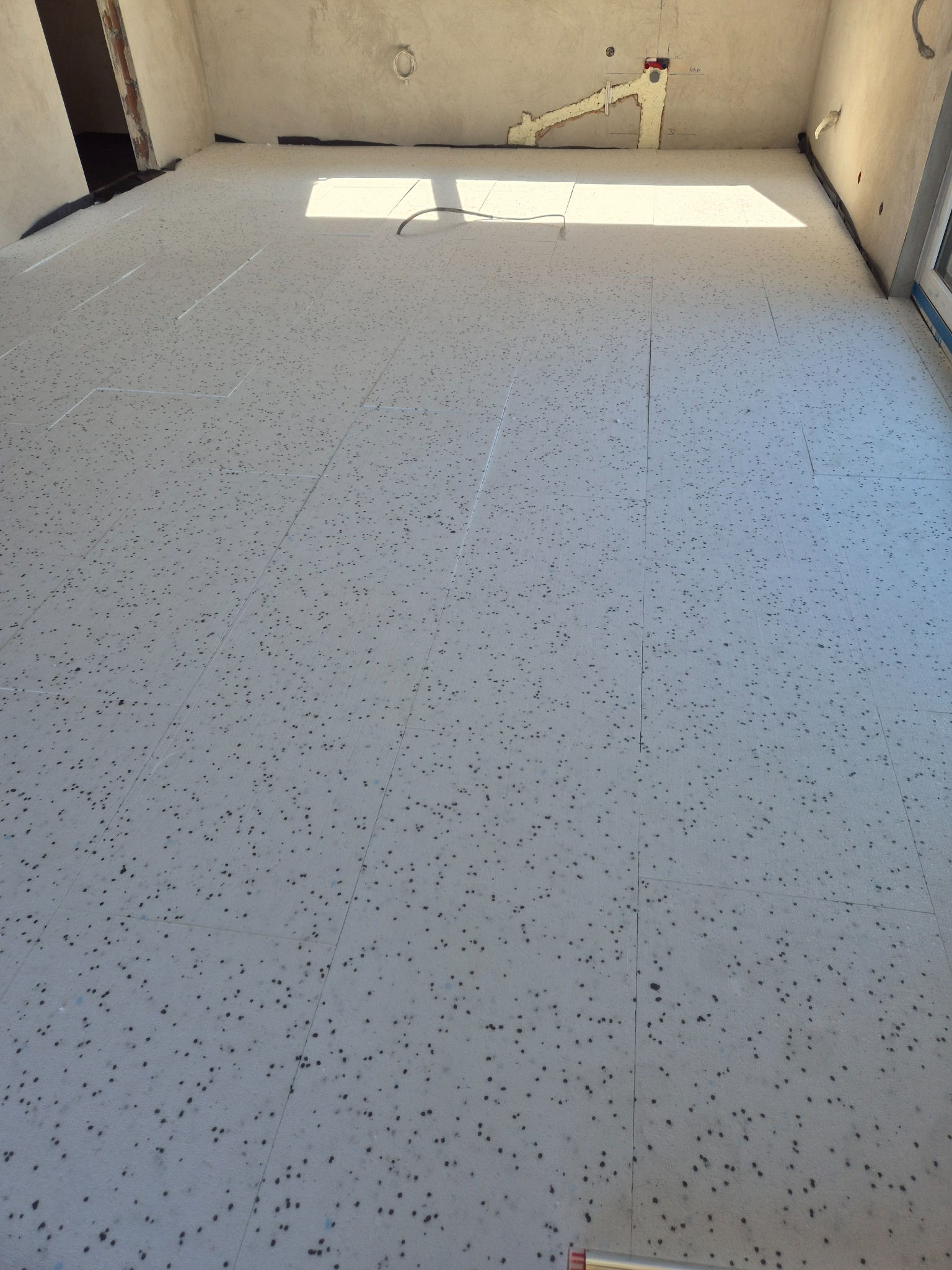 Przygotowanie podłoża: rozłożone płyty izolacyjne z charakterystycznym wzorem kropek na podłodze w surowym wnętrzu przed dalszymi pracami instalacyjnymi.