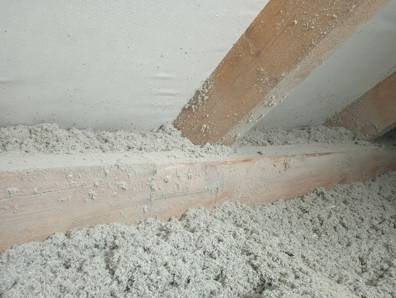 Poddasze z drewnianą konstrukcją krokwiową wypełnione szarą wełną celulozową, widoczna membrana paroizolacyjna na górze.