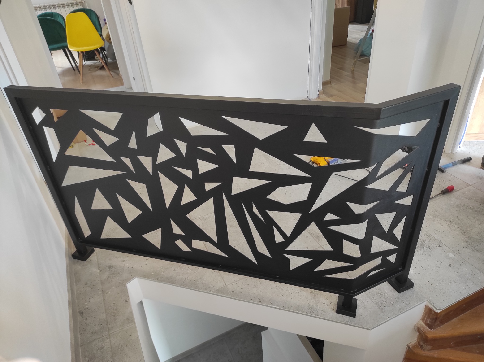 Nowoczesna, czarna balustrada z geometrycznym wzorem trójkątów, zamontowana na schodach wewnątrz budynku, widok z góry.