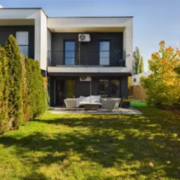 Nowoczesny, dwukondygnacyjny dom z ogrodem w Chorzowie, z balkonem i tarasem. Widoczne krzewy i drzewa w jesiennych barwach. Minimalistyczny design.