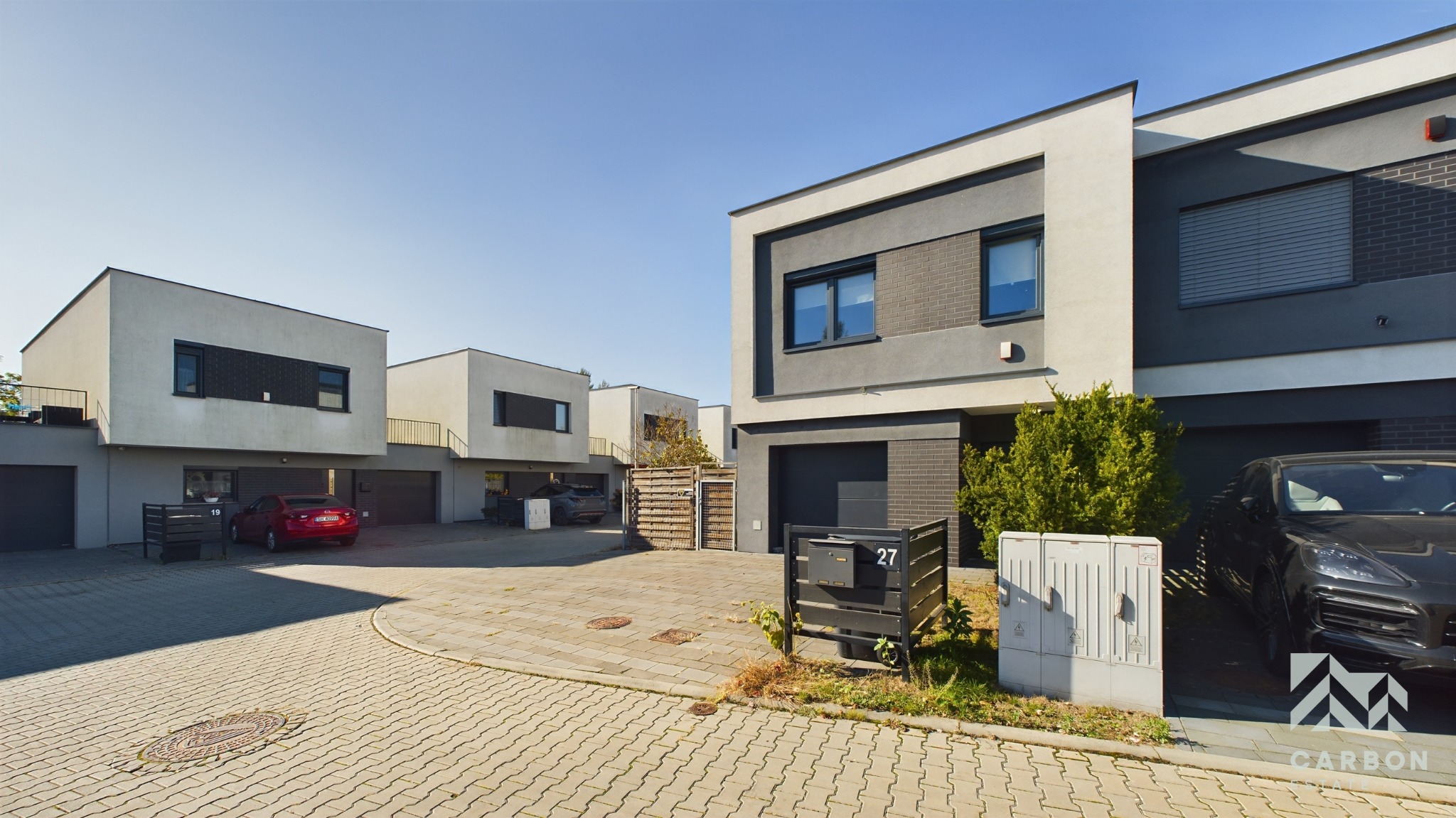 Nowoczesne szeregówki z garażami w Chorzowie. Minimalistyczna architektura, kostka brukowa, skrzynki pocztowe. Domy w odcieniach szarości i bieli, auta na podjazdach.