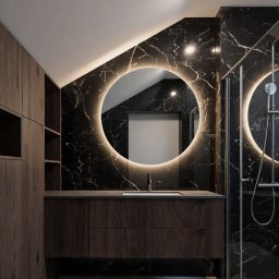 Studio Sawubona - Nowoczesna łazienka na poddaszu z czarnymi marmurowymi płytkami, okrągłym lustrem z podświetleniem LED i drewnianymi szafkami. Minimalistyczny design, kabina prysznicowa.