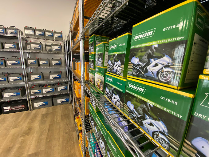 Półki magazynowe wypełnione rzędami akumulatorów samochodowych w szarych pudełkach oraz zielonych pudełkach z ilustracją motocykla; widok z perspektywy pod lekkim kątem.