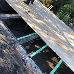 PVK Group Sp z o p - Montaż nowych desek na konstrukcji dachu, widoczne stare deski i elementy konstrukcyjne, młotek leżący na nowej powierzchni, praca w toku.