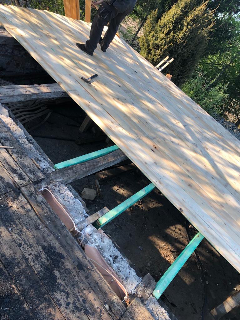 Montaż nowych desek na konstrukcji dachu, widoczne stare deski i elementy konstrukcyjne, młotek leżący na nowej powierzchni, praca w toku.