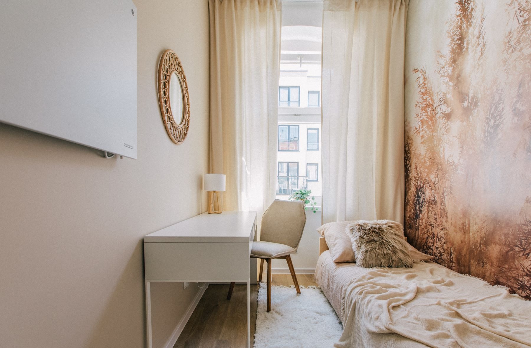 Jasny pokój z biurkiem, łóżkiem i fototapetą z motywem lasu, oświetlony naturalnym światłem wpadającym przez okno z kremowymi zasłonami.