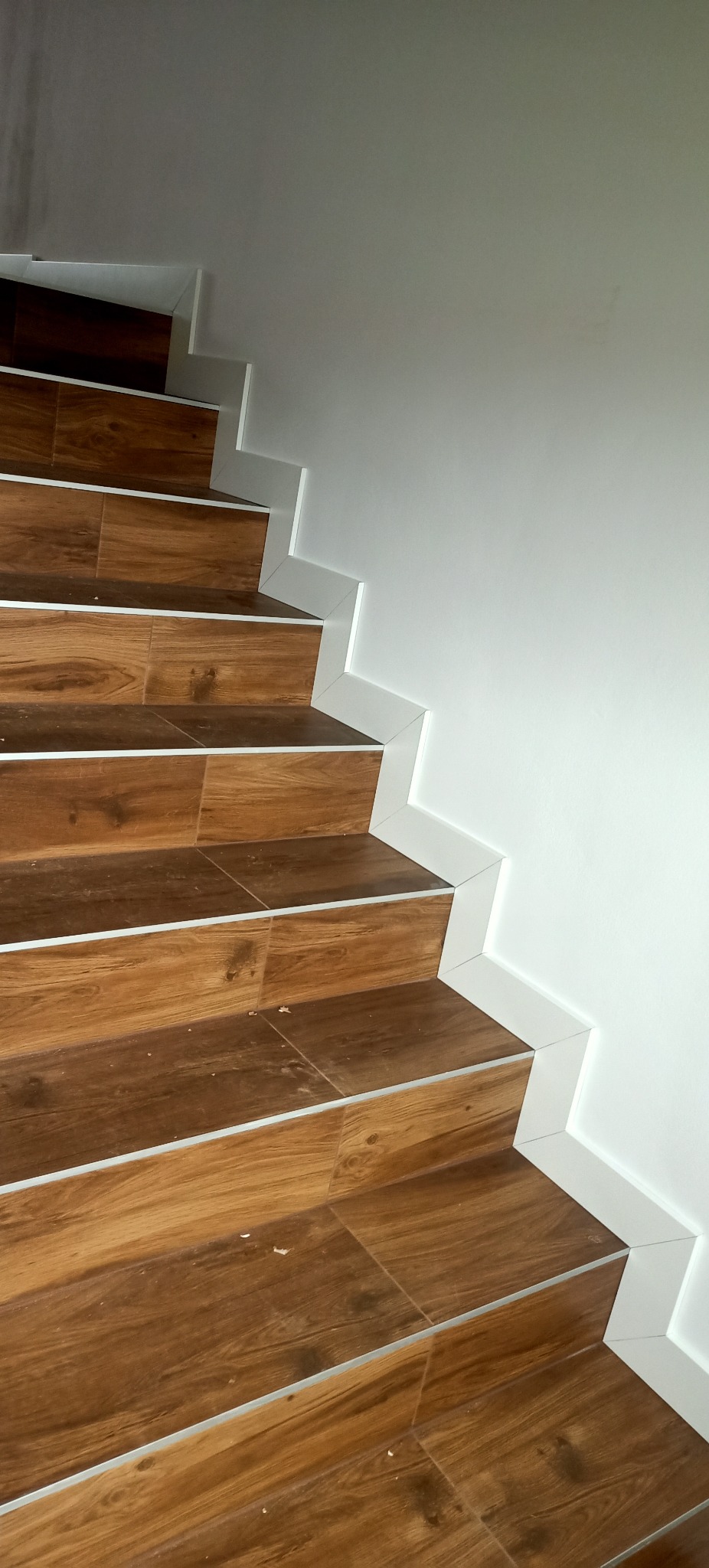 Schody wyłożone brązowymi płytkami imitującymi drewno, z białymi listwami przypodłogowymi, widok z dołu.