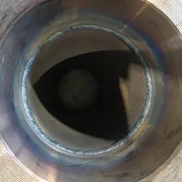 Wewnętrzny widok spawu na metalowej rurze. Widoczne ślady termiczne po spawaniu i rowkowana powierzchnia metalu. Spaw wykonany z dużą precyzją.