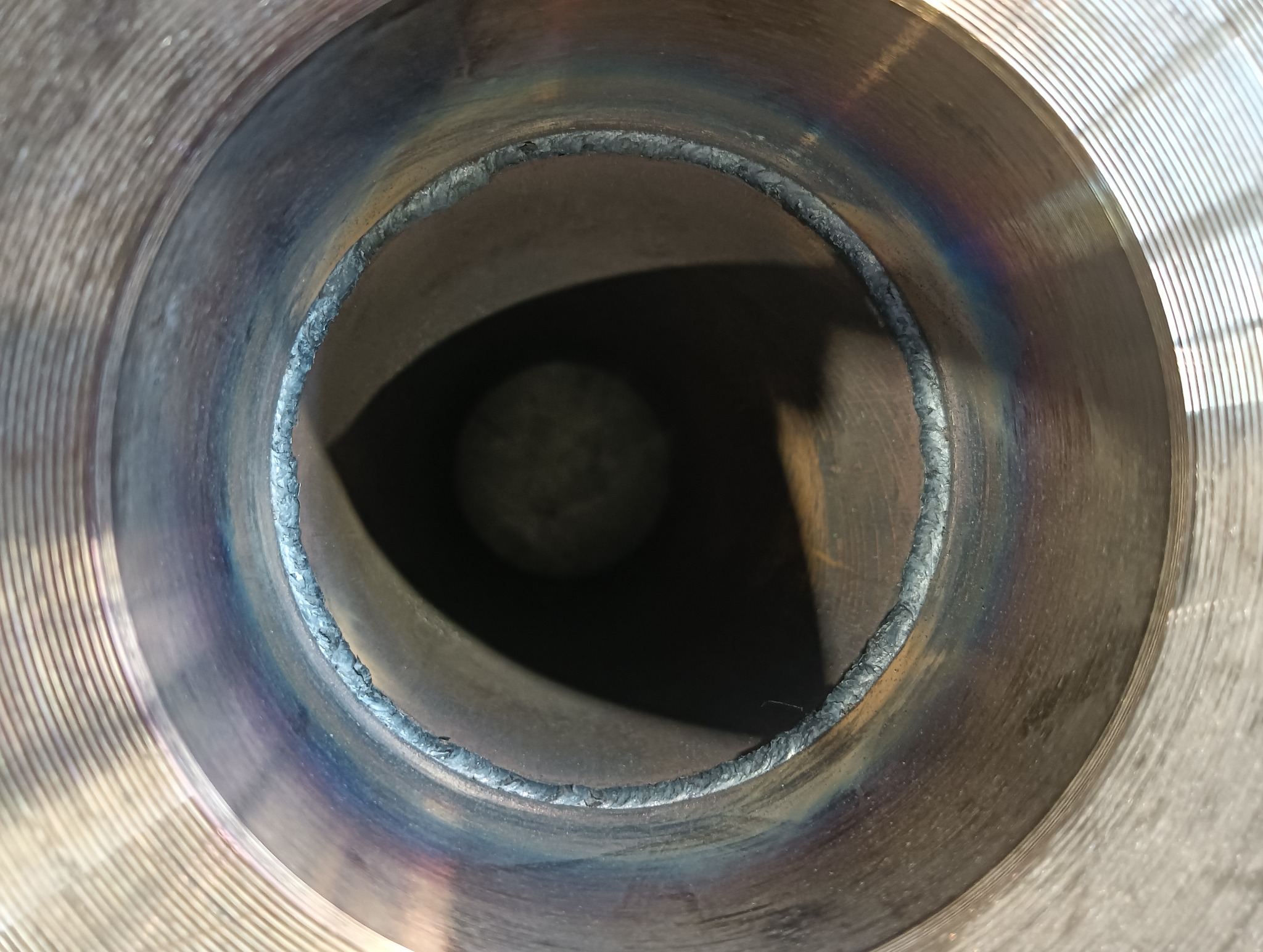 Wewnętrzny widok spawu na metalowej rurze. Widoczne ślady termiczne po spawaniu i rowkowana powierzchnia metalu. Spaw wykonany z dużą precyzją.