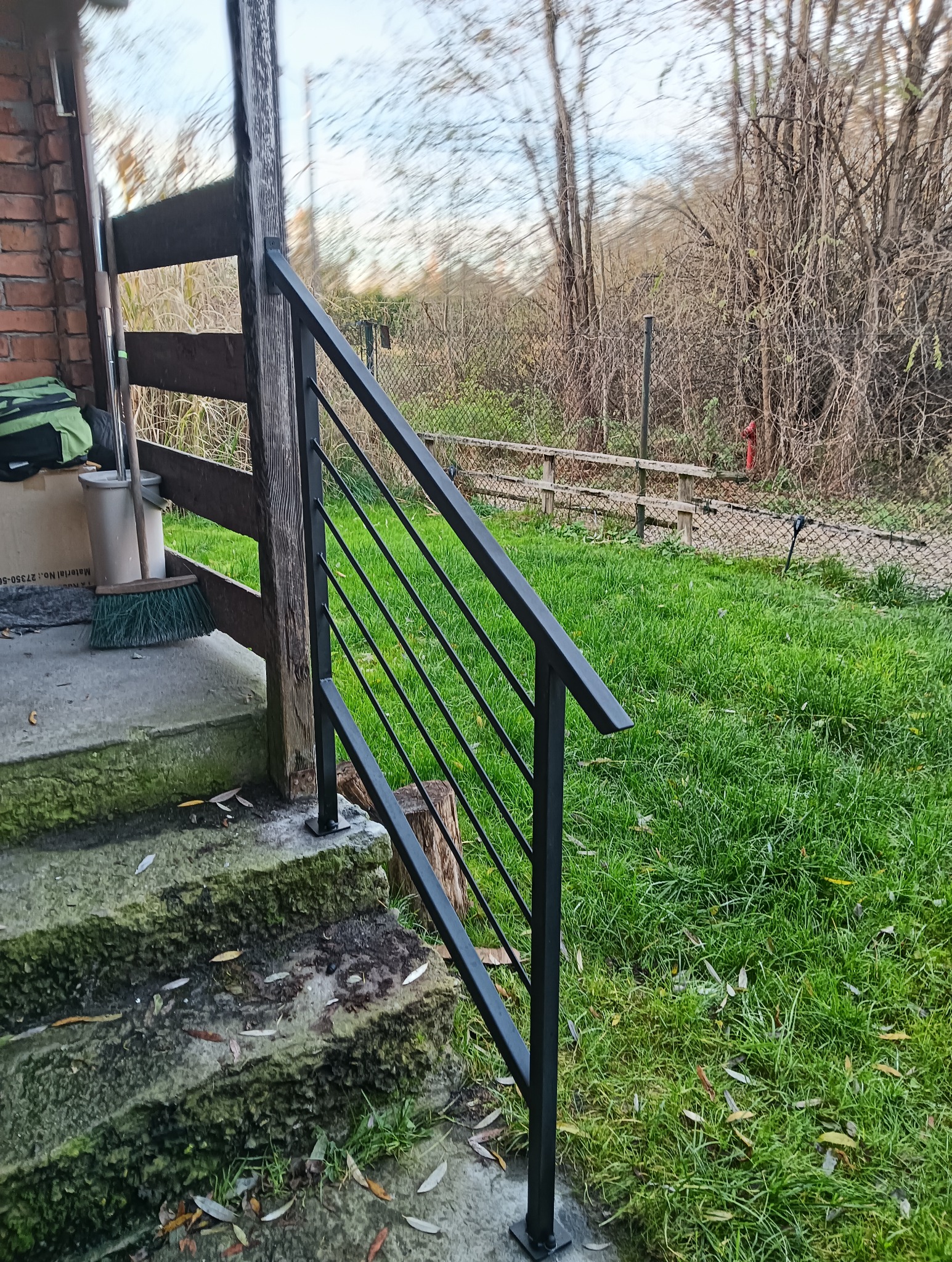 Nowoczesna, czarna konstrukcja przy schodach wejściowych w Rudawie. Minimalistyczny design, widoczne detale mocowania. Trawa i zieleń w tle.