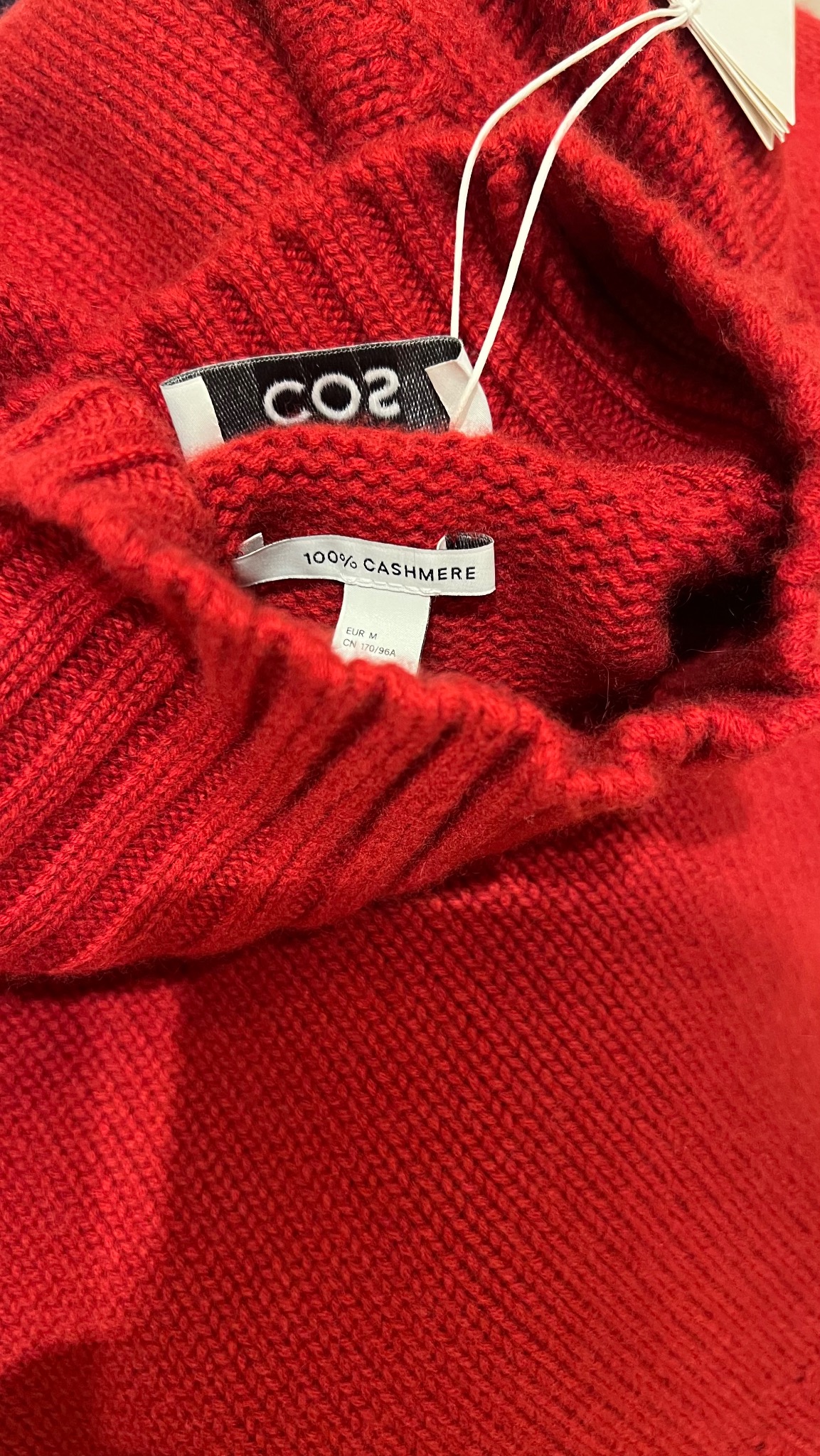 Czerwony kaszmirowy sweter z metkami marki COS i informacją o składzie: 100% kaszmir.