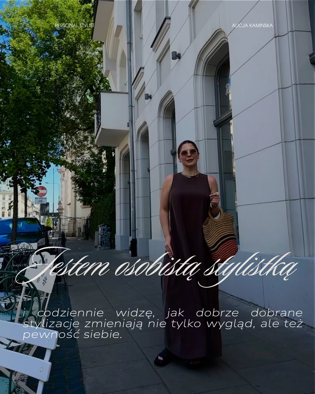 Kobieta w długiej sukience pozuje na tle miejskiej architektury. Uwagę przyciągają okulary w stylu retro i torebka z naturalnych materiałów. Ujęcie z dołu.