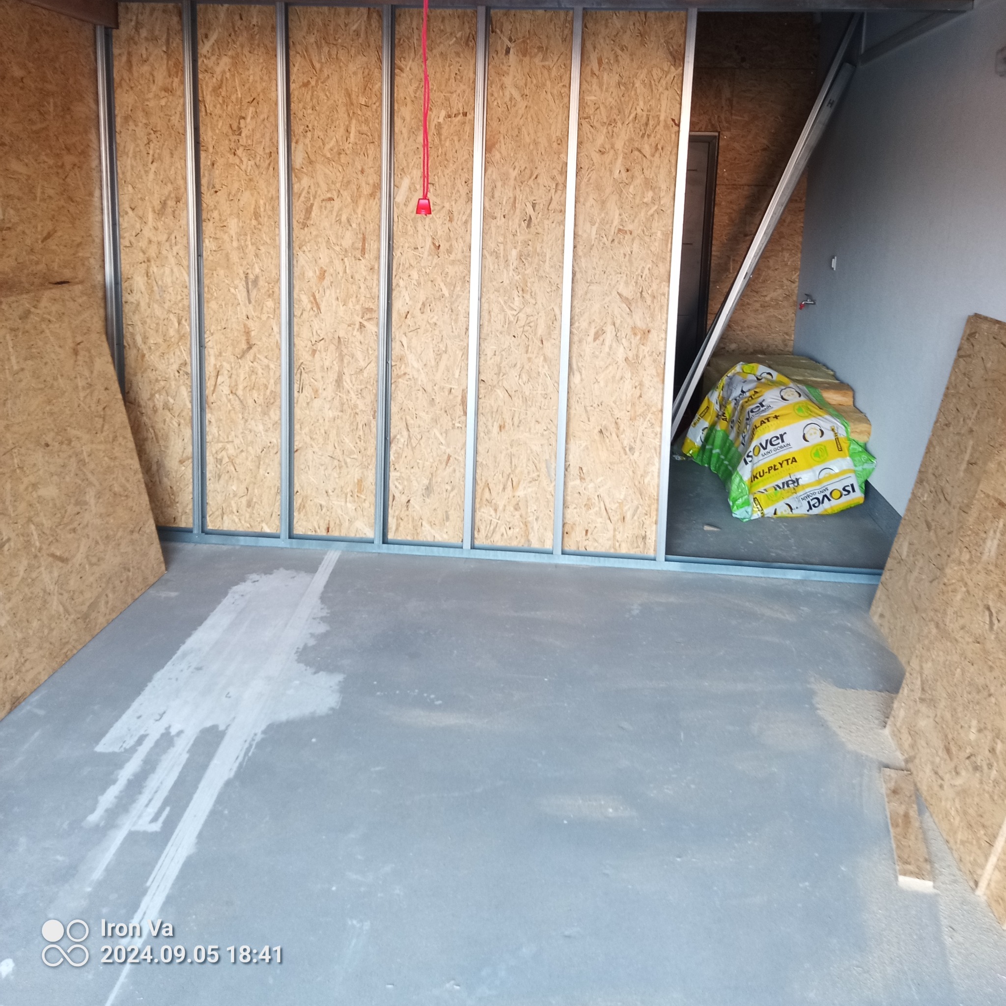 Wnętrze w trakcie prac remontowych: ściany z płyt OSB na metalowej konstrukcji, paczki wełny mineralnej Isover w tle, surowa wylewka na podłodze.