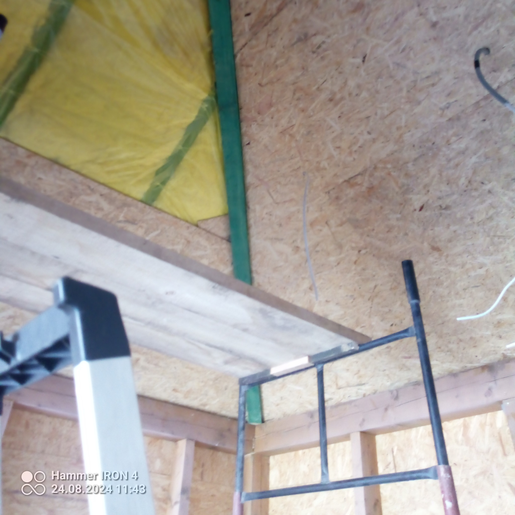 Sufit poddasza z izolacją z wełny mineralnej, widoczne elementy konstrukcyjne i fragment rusztowania.