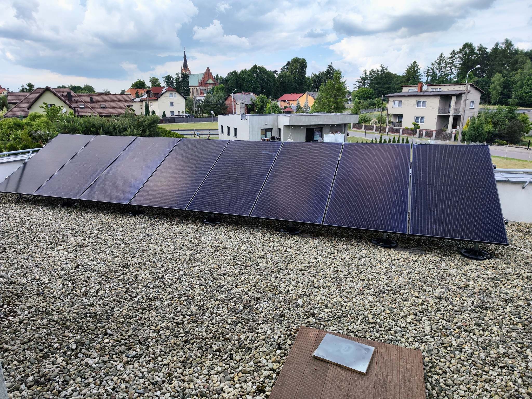 Panel słoneczny na żwirowym dachu z widokiem na miasteczko i kościół w tle.