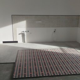 Serra's team Zakład Budowlany Rafał Serafin - Wnętrze kuchni w trakcie prac wykończeniowych: ułożona podłoga z wzorzystych płytek, częściowo wykończona ściana nad blatem z dekoracyjnymi kaflami i widoczne instalacje.