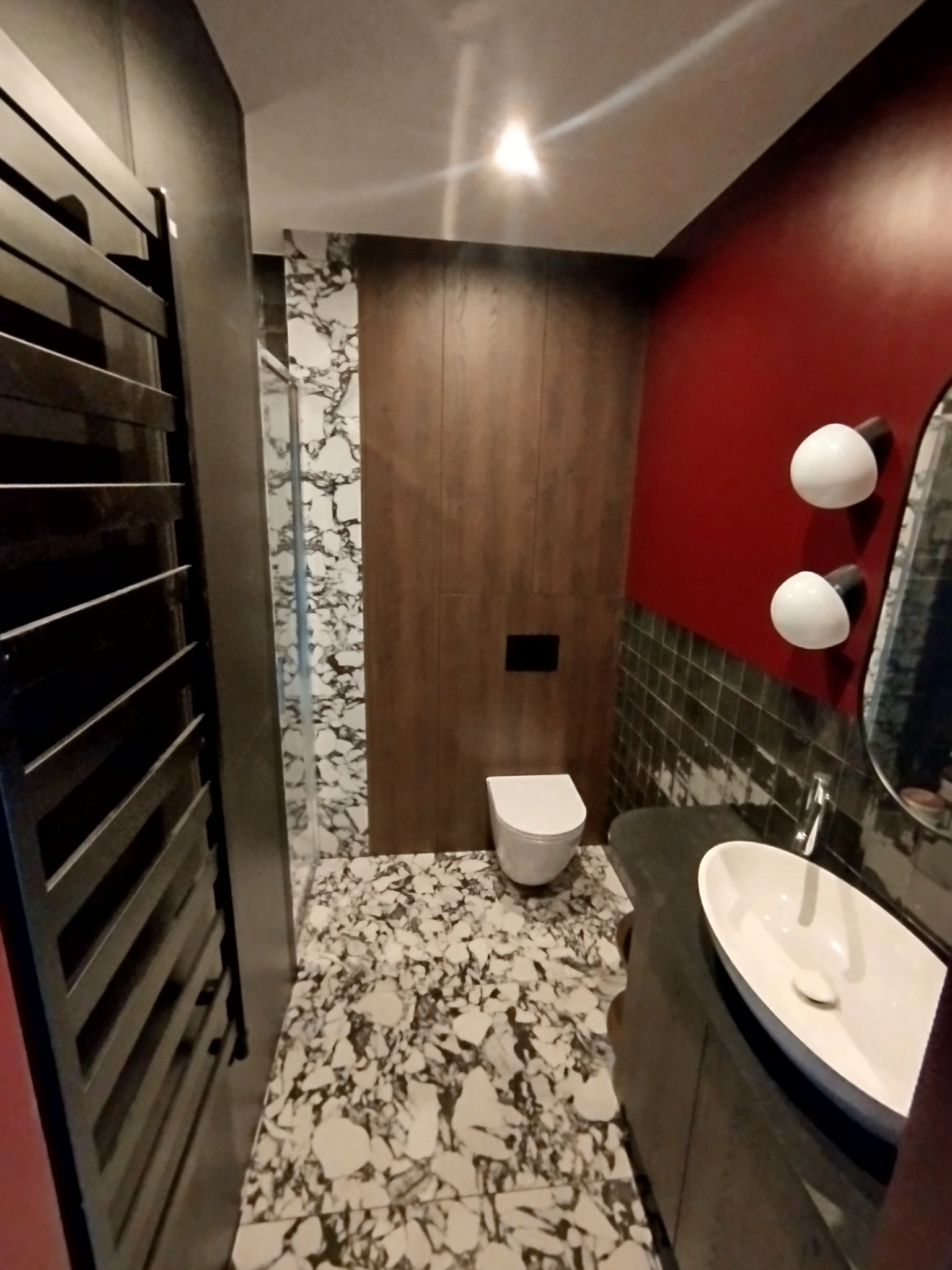 Nowoczesna łazienka z marmurową podłogą i ścianą prysznicową, drewnianymi panelami, czerwoną ścianą, owalną umywalką i grzejnikiem drabinkowym.