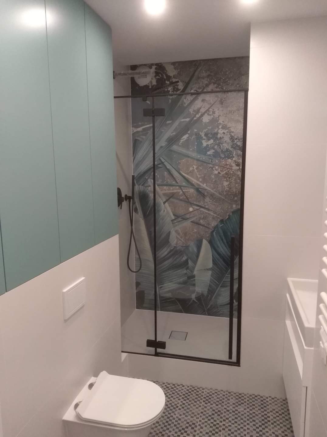 Nowoczesna łazienka z kabiną prysznicową typu walk-in, płytki z motywem roślinnym na ścianie, szafka w kolorze miętowym i mozaika na podłodze.