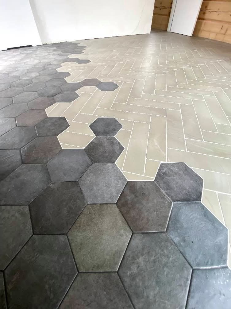 Ukończona podłoga z heksagonalnych, szarych płytek przechodzących w jasne, prostokątne ułożone w jodełkę. Nietypowe połączenie wzorów i kolorów na podłodze.