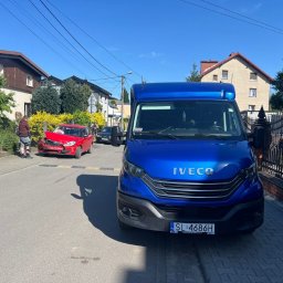 Pomoc drogowa Laweta 24h-OnlyCars - Niebieski samochód dostawczy Iveco na ulicy, w tle uszkodzony czerwony samochód osobowy po kolizji, osoba z ortezą na nodze przygląda się uszkodzeniom.