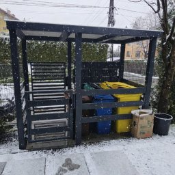 AR-Gelender Radosław Mojżyszek - Metalowa konstrukcja z zamykaną furtką, osłaniająca pojemniki na odpady w kolorach: żółtym, niebieskim i brązowym. Zimowy krajobraz, padający śnieg.