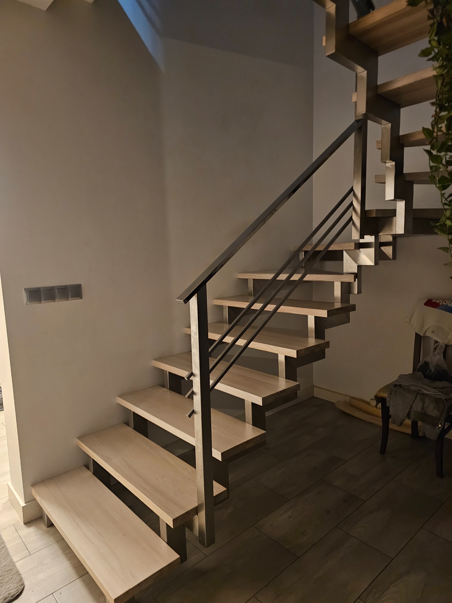 Nowoczesne schody drewniane z metalową balustradą, oświetlone naturalnym światłem, widoczne z dołu, z minimalistycznym wykończeniem wnętrza.