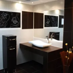 Nowoczesna łazienka w tonacji czerni i bieli z dekoracyjnymi panelami z motywem kwiatowym, asymetryczna umywalka na blacie, minimalistyczna szafka pod umywalką i wazon z suszonymi kwiatami.