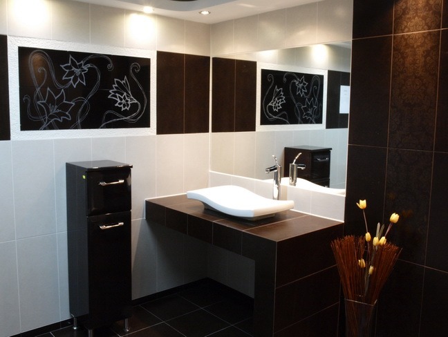 Nowoczesna łazienka w tonacji czerni i bieli z dekoracyjnymi panelami z motywem kwiatowym, asymetryczna umywalka na blacie, minimalistyczna szafka pod umywalką i wazon z suszonymi kwiatami.