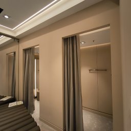 Pruzo Marek Strzała - Przymierzalnia w neutralnych barwach z szarymi zasłonami, widoczna podłoga zabezpieczona folią ochronną.