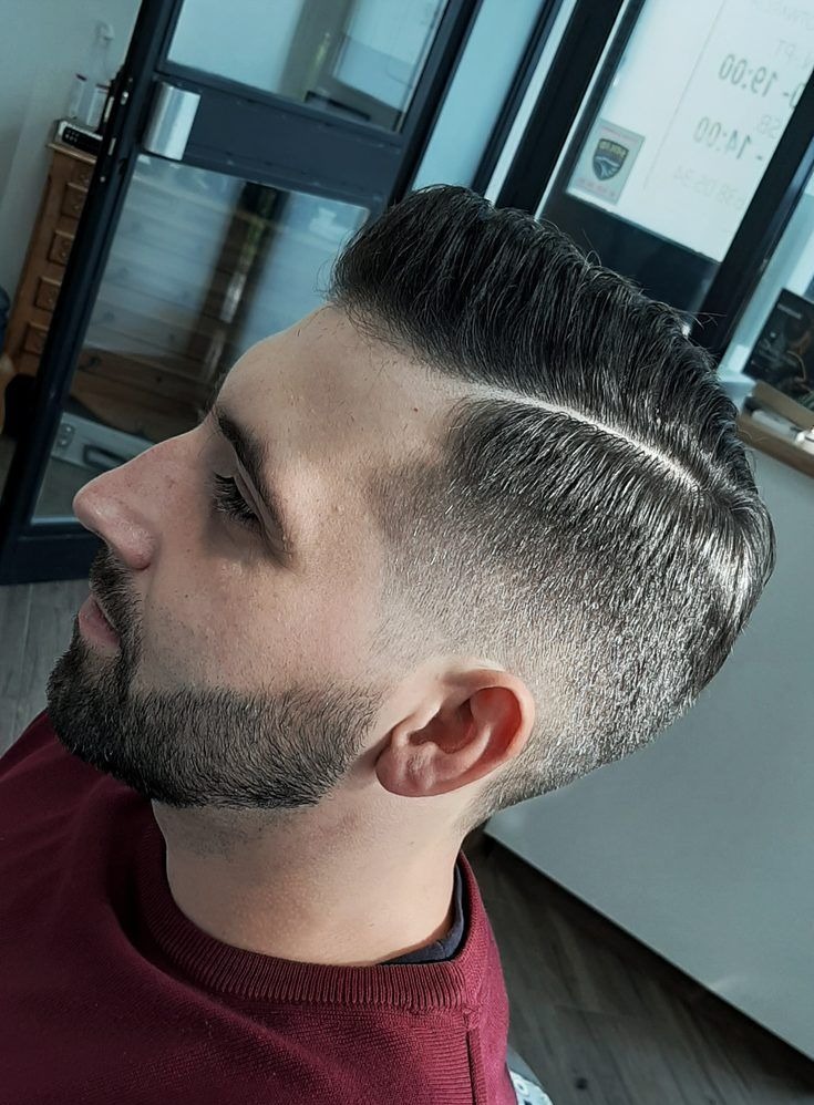 Męska fryzura z wyraźnym przedziałkiem, cieniowaniem po bokach i starannie przystrzyżoną brodą, widok z profilu.