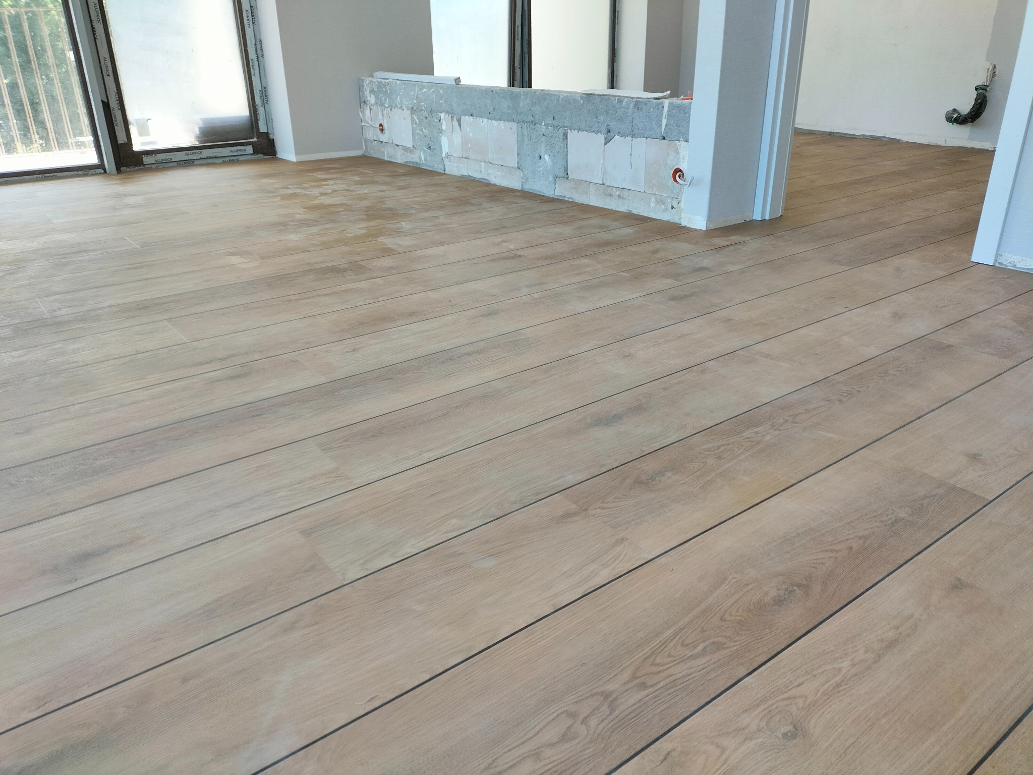 Jasne panele podłogowe ułożone w nowym mieszkaniu, widoczne ślady po budowie, w tle niedokończona ściana działowa z pustaków.