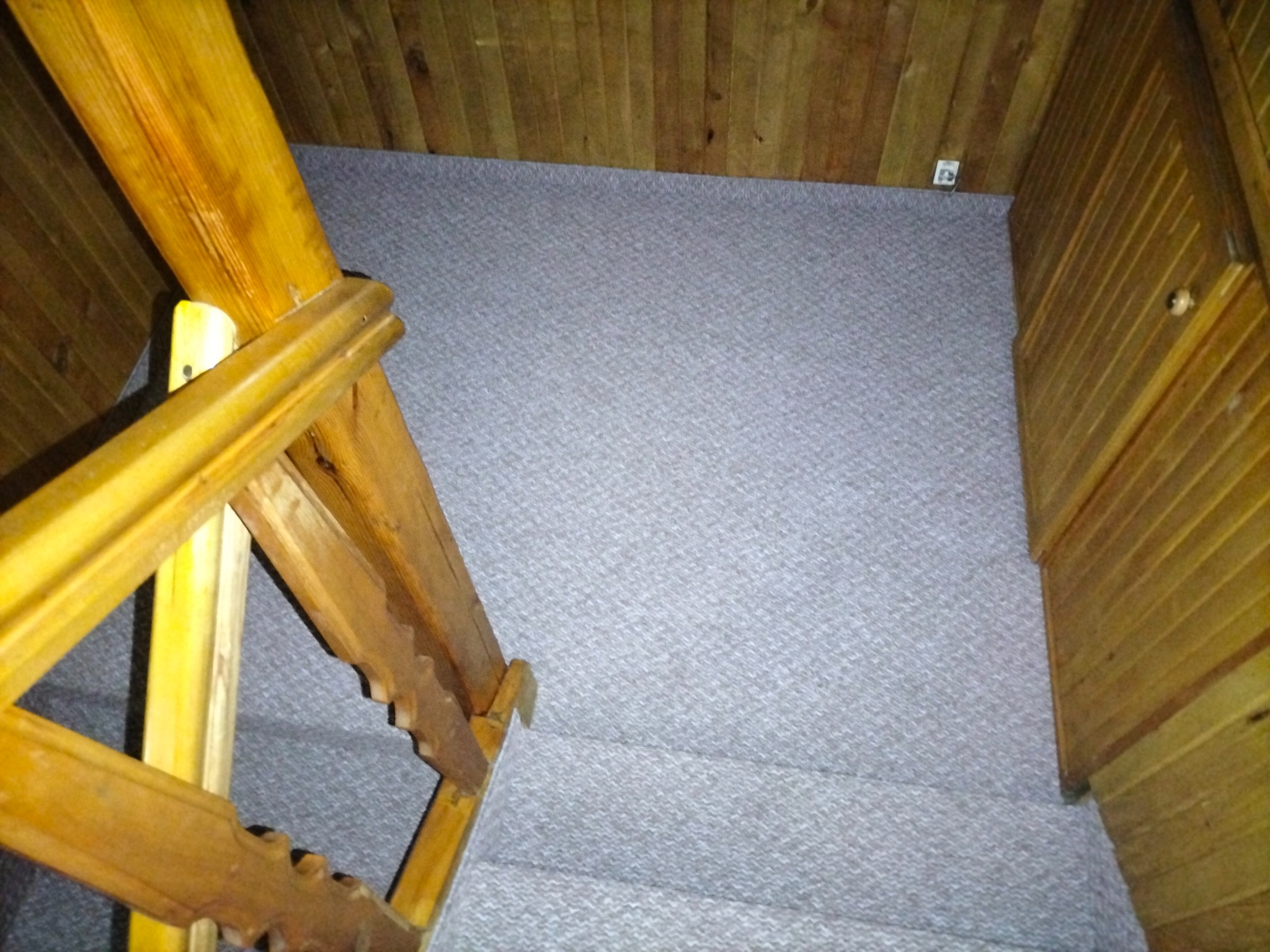 Szara wykładzina dywanowa na schodach z drewnianą barierką i boazerią ścienną.