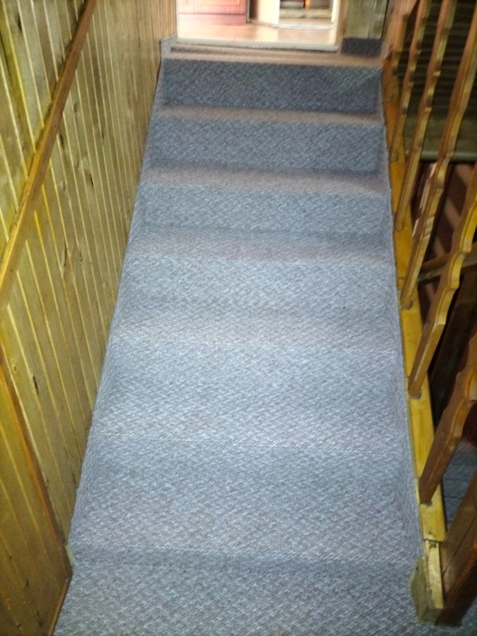 Szare pokrycie schodów wykładziną dywanową, widok z góry, drewniane barierki po obu stronach.